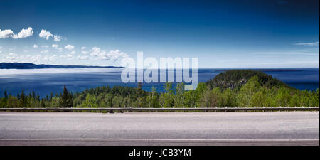 Panorama of Trans-Canada highway with blue sky over misty Lake Superior nature scenery in the background. Ontario, Canada. Stock Photo