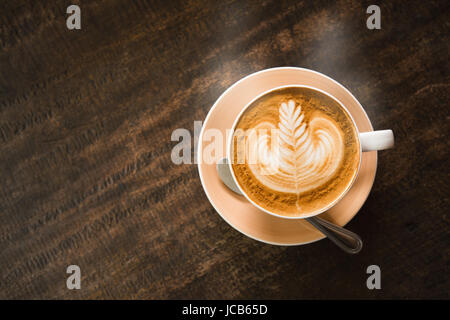 Close focus on cup of hot cappuccino coffee with latte art on dark brown wood table. Stock Photo