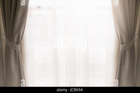 Opened silk curtain in cream color on window covering by see through white curtain with bright light from outside. Stock Photo