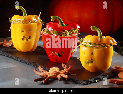 Halloween themed salad with stuffed red and yellow sweet peppers with cutout faces like jack-o-lanterns served with a flying bat pastry on a curved bark plate Stock Photo