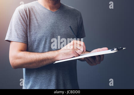 Casual adult male writing notes on notepad paper, unrecognizable guy in gray t-shirt with pencil Stock Photo