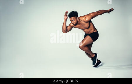 Studio shot of fit young man running over grey background. African american male model with muscular body. Stock Photo