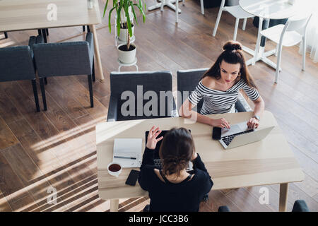 Two women chat to each other in the office with one woman having her laptop. Stock Photo