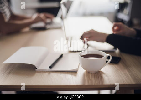 Shot of a woman's hands typing on a laptop keyboard, with a cup of hot coffee near. Stock Photo