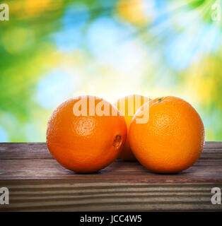 Oranges on wooden table over shiny leaves background Stock Photo