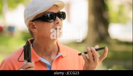 Hispanic blind man with disability. Visually impaired man using Digital Assistant and Ease of Access functions on mobile phone, voice typing to smartp Stock Photo