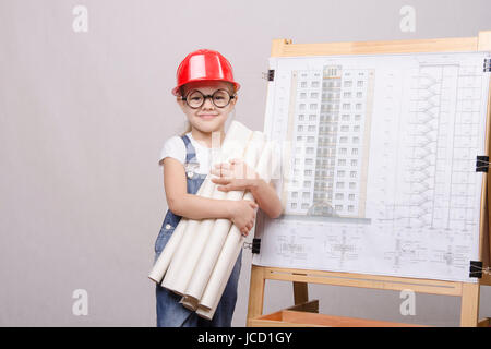 Girl Builder, architect, holding a bunch of drawings, standing at the blackboard with the drawing of the building Stock Photo