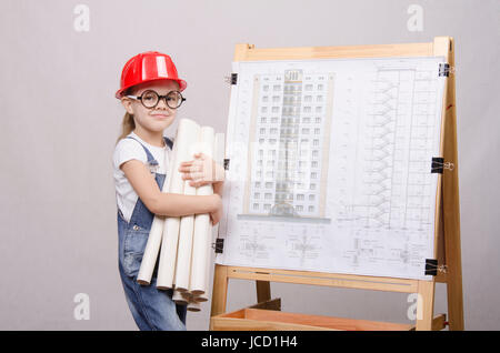 Girl Builder, architect, holding a bunch of drawings, standing at the blackboard with the drawing of the building Stock Photo