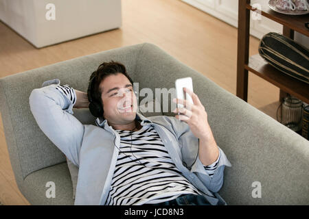 Smiling western man using smartphone relaxing on sofa Stock Photo