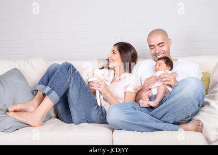 Young parents with little baby at home, sitting on cozy divan, enjoying family, loving couple with newborn daughter, positivity and fun concept Stock Photo