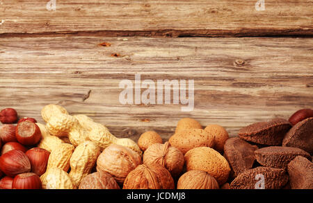 Border of assorted whole nuts in their shells including almonds, hazelnuts, brazil nuts, peanuts and walnuts on textured rustic wood with copyspace Stock Photo