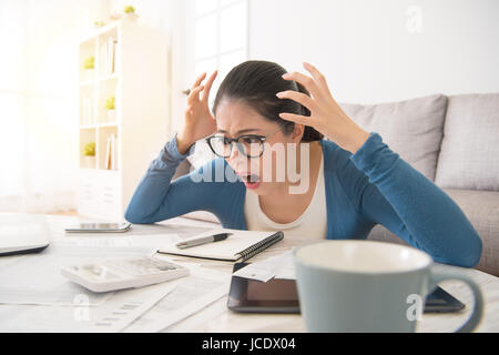 shocked crazy woman checking expensive electricity and household bills sitting on sofa in the living room at home. finance interior and domestic house Stock Photo