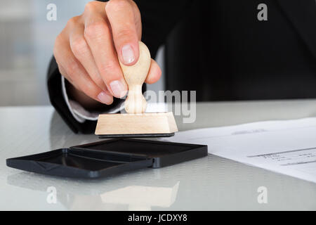Close-up Of Business Man Hand Pressing Rubber Stamp On Document Stock Photo