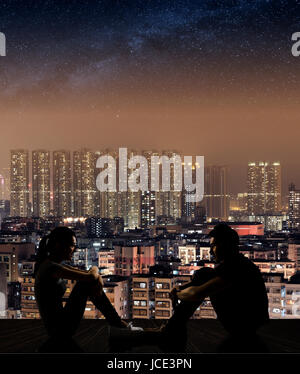 Silhouette of young couple face to face sit on ground in the city night. Stock Photo