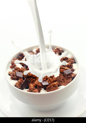 Pouring milk with a splash of droplets into a bowl of crunchy choc chip breakfast cereal rich in wheat, oats and bran for an energising low-CI start to the day Stock Photo