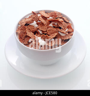 Bowl of crispy flakes of chocolate flavored breakfast cereal in milk for a tasty nutritional meal served in a white ceramic bowl and saucer , in square format Stock Photo