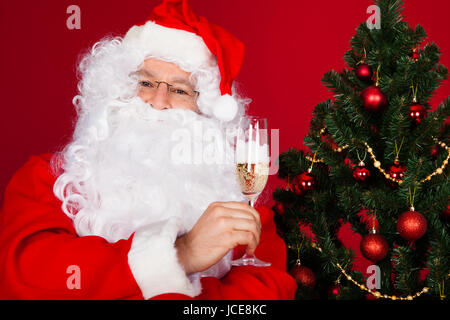 Portrait of a happy santa holding wine glass over red background Stock Photo