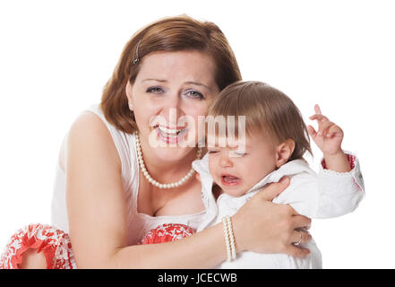 Young baby who is upset and crying being cuddled in its mothers arms as she laughs at the camera Stock Photo