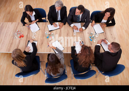Overhead view of a group of professional business people in a meeting seated around a wooden table with their notepads Stock Photo
