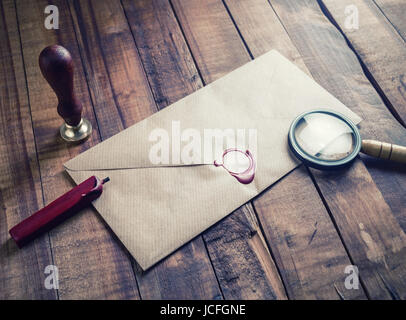 Photo of craft paper envelope, magnifier, seal and stamp on wood background. Vintage still life with postal accessories. Blank stationery.