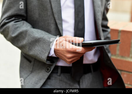 closeup of a young caucasian businessman in a gray suit using a tablet outdoors Stock Photo