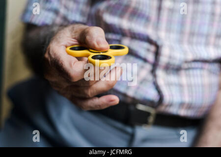 closeup of an old caucasian man playing with a yellow fidget spinner Stock Photo