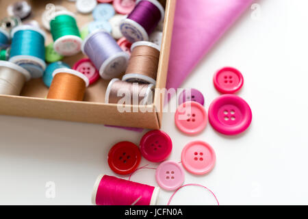 box with thread spools and sewing buttons on table Stock Photo