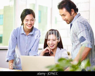a team of young and cheerful asian business executives working together in office using laptop computer. Stock Photo