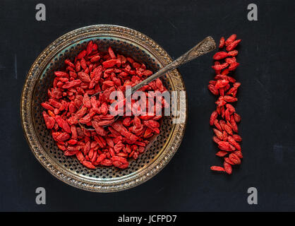 Raw dried goji berries on a vintage metal plate with spoon on a black scratched background Stock Photo