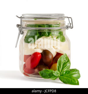 Fresh farm style layered caprese salad in an closed lid mason jar before adding dressing with basil sprig in front isolated on white. Stock Photo