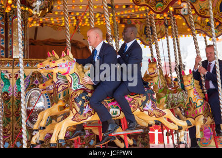 Group of friends wearing suits and dresses on a merry-go-round on the seafront at Brighton on a sunny day. It looks as if they are part of a wedding. Stock Photo