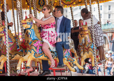Group of friends wearing suits and dresses on a merry-go-round on the seafront at Brighton on a sunny day. It looks as if they are part of a wedding. Stock Photo