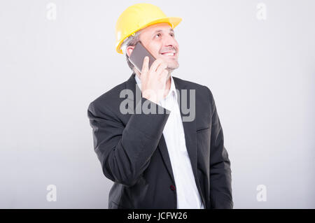 Portrait of architect smiling and talking on smartphone wearing yellow hardhat on grey background Stock Photo