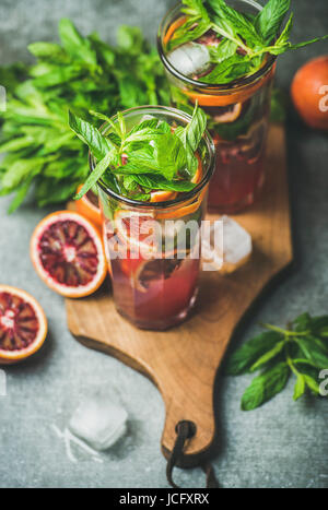 Blood orange citrus lemonade with fresh mint and ice cubes in tall glasses on wooden board over dark brown stone background. Refreshing summer drink c Stock Photo