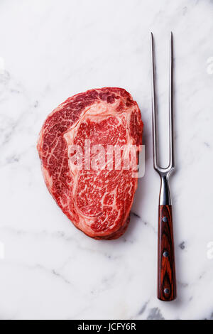 Raw fresh marbled meat Steak Ribeye Black Angus and meat fork on white marble background copy space Stock Photo