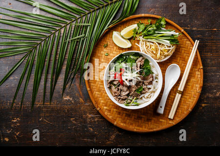 Pho Bo vietnamese Soup with beef on bamboo tray and palm branch on wooden background Stock Photo