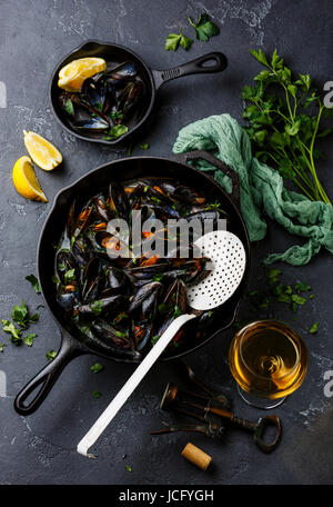 Mussels in black cooking pan with parsley and wine on dark stone background Stock Photo