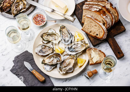 Open shucked Oysters with bread, butter and champagne on white marble background Stock Photo
