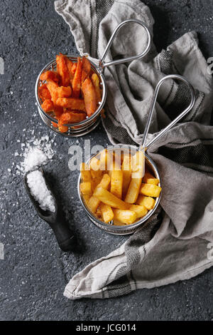 Variety of french fries traditional potatoes, sweet potato, carrot served with white salt, thyme in frying basket over dark texture background. Top vi Stock Photo