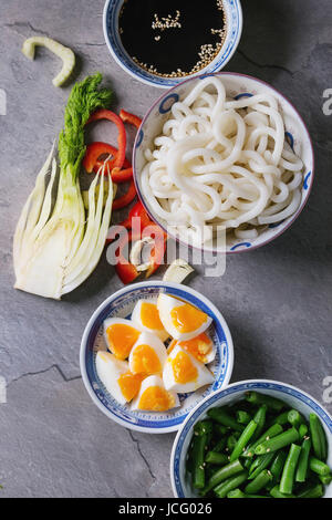 Ingredients for cooking stir fry udon noodles, green beans, sliced paprika, boiled eggs, soy sauce with sesame seeds in traditional bowls with wooden 