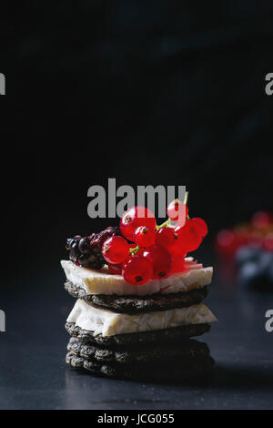 Black charcoal crackers with camembert brie cheese and berries blueberry, dewberry, red currant and sliced figs, served on vintage tray over dark meta Stock Photo