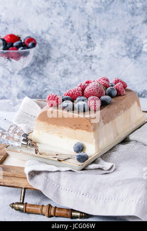 Three layers vanilla, coffee and chocolate ice cream cake, served with frozen berries and macaroons biscuits on rectangular white plate, textile napki Stock Photo
