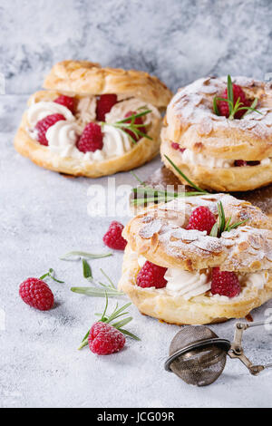 Homemade choux pastry cake Paris Brest with raspberries, almond, sugar powder and rosemary, served over gray blue texture background. Close up. French Stock Photo