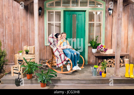 mother and daughter sitting in rocking chair and hugging on porch Stock Photo