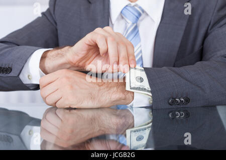 Close-up Of Businessperson Pulling Out Bank Note From Sleeve At Workplace Stock Photo