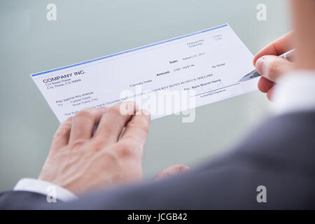 Close-up Of Businessperson Signing Money Cheque With Pen Stock Photo