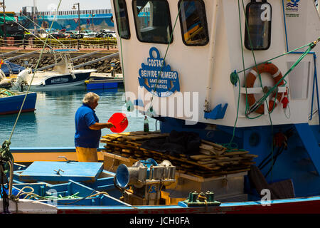 A deck hand works on a local fishing trawler berthed in the crowded harbor in Los Cristianos in Spanish Island of Teneriffe Stock Photo