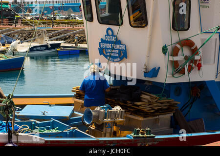 A deck hand works on a local fishing trawler berthed in the crowded harbor in Los Cristianos in Spanish Island of Teneriffe Stock Photo