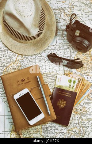 A travel concept image with an instant camera, mobile phone, sunglasses, various world currencies, and a white hat on an ancient map, vintage effect Stock Photo