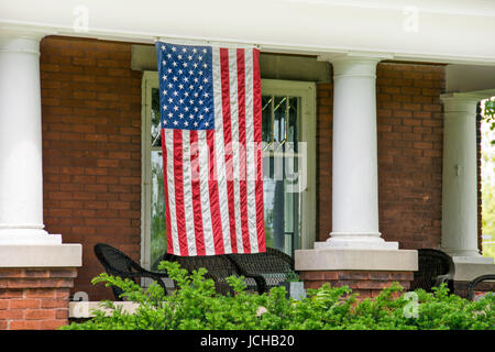 American flag hanging on front porch of old brick home with white pillars Stock Photo